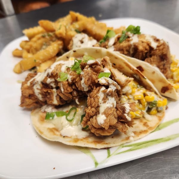 Crispy chicken tacos with corn salsa, drizzled with white sauce, served with fries.