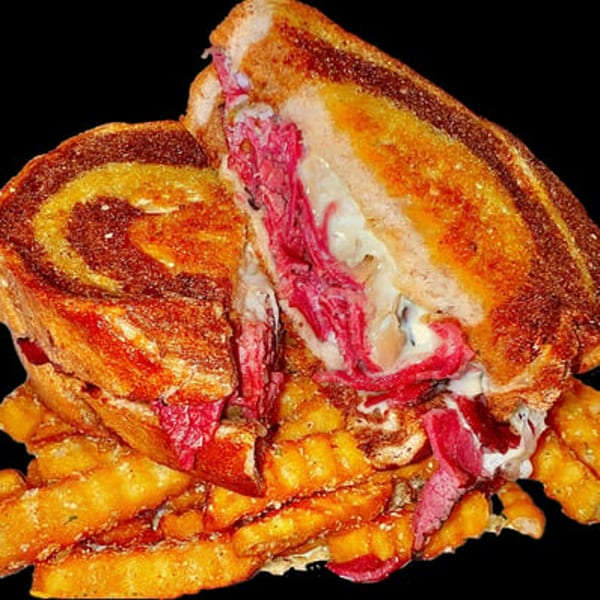 A grilled sandwich with pastrami and melted cheese, cut in half, served with golden fries.