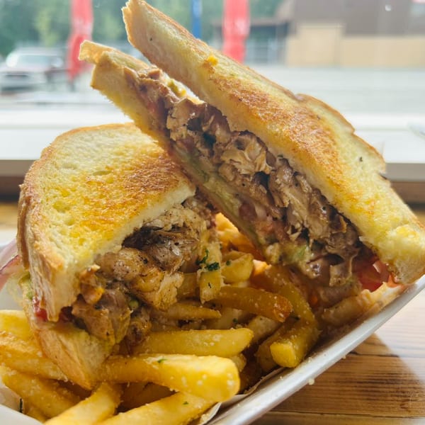 A grilled chicken sandwich, cut in half, with fries on a white plate at Main Event Grill.