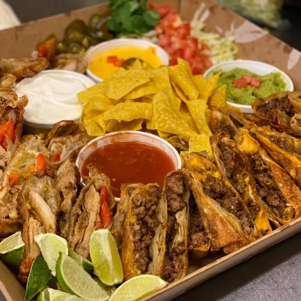 A platter of Main Event Grill's crispy egg rolls, nachos, and various dips.